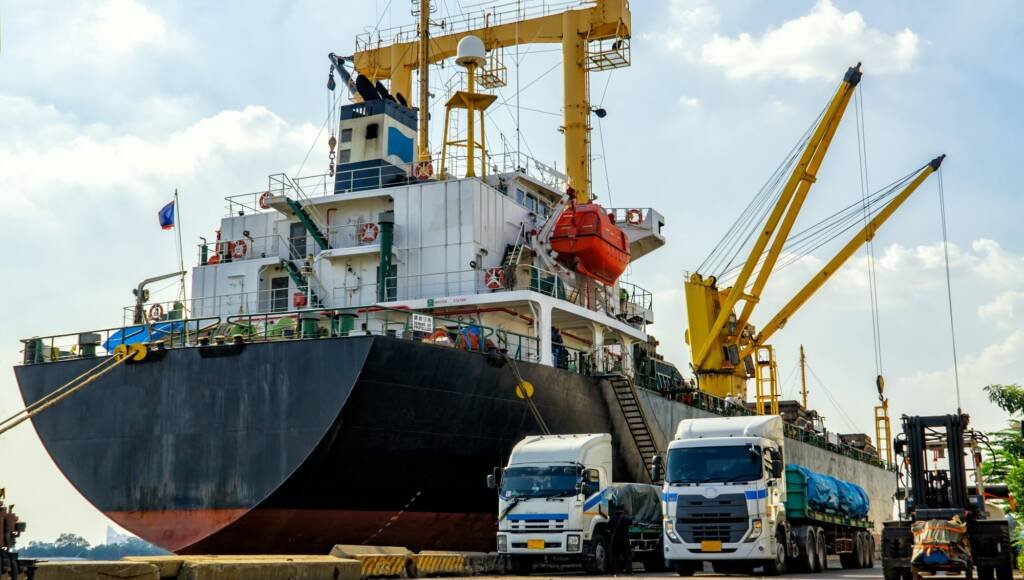 Export container ship with cranes loading goods on trucks